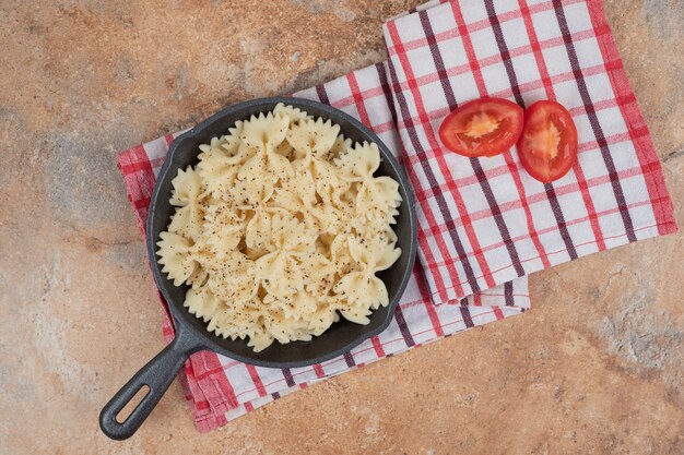 Farfalle sur poêle noir avec des tranches de tomates. Illustration de haute qualité