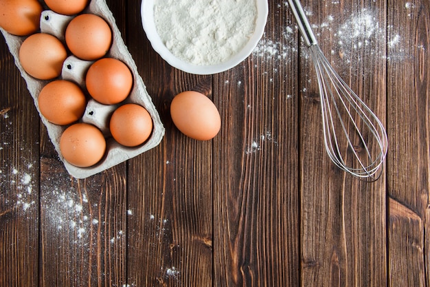 Farine dans un bol avec des œufs, fouetter à plat sur une table en bois