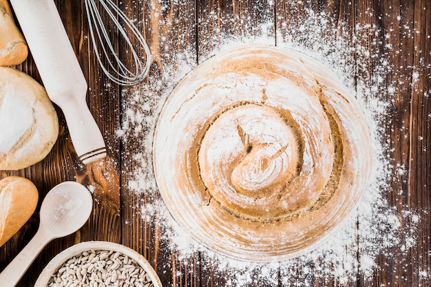 De la farine éclaboussée sur le tourbillon du pain rond avec un rouleau à pâtisserie et une moustache sur la table