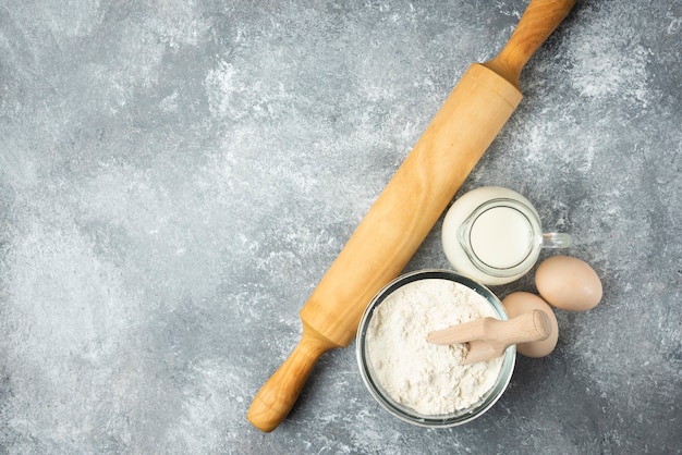 Photo gratuite farine, œufs, lait et rouleau à pâtisserie sur marbre.