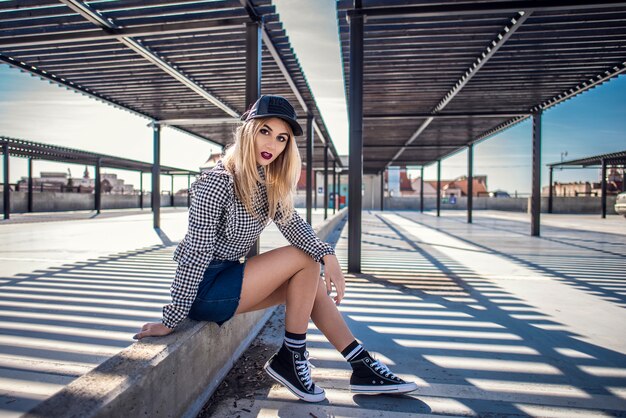 Fashion hipster femme assise sur un mur en béton avec des baskets