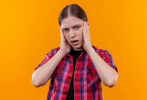 Fatigué de belle jeune fille portant une chemise rouge a mis ses mains sur la joue sur un mur jaune isolé