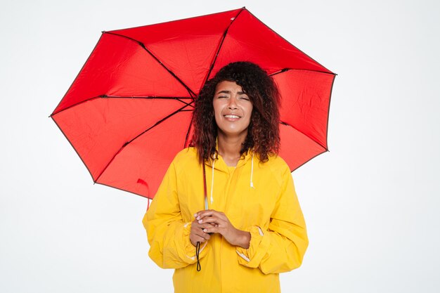 Fatigué femme africaine en imperméable pleurer tout en se cachant sous un parapluie