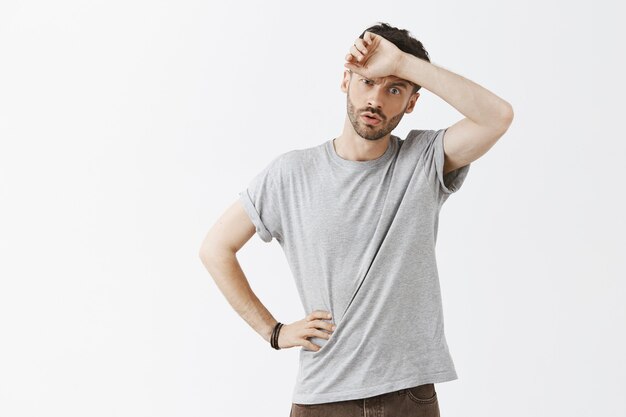 Fatigué jeune beau mec posant contre le mur blanc