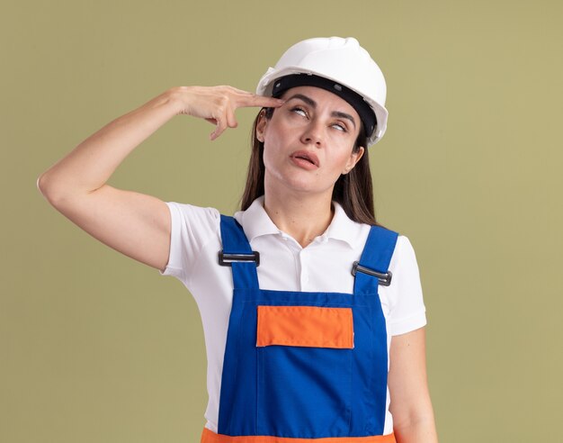 Fatigué de jeune femme en uniforme montrant le suicide avec un geste de pistolet isolé sur un mur vert olive