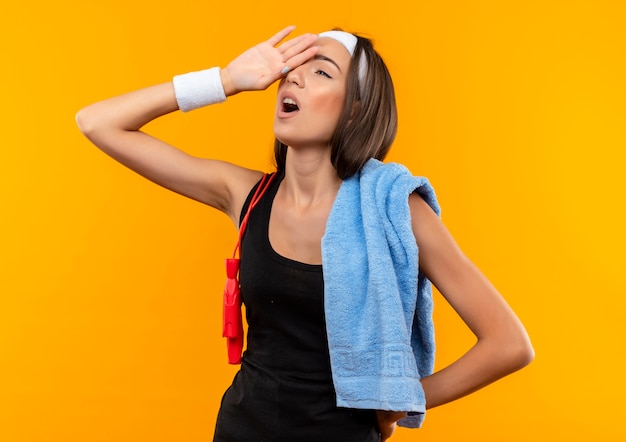 Fatigué de jeune fille assez sportive portant bandeau et bracelet avec serviette et corde à sauter sur ses épaules mettant la main sur la tête sur l'espace orange