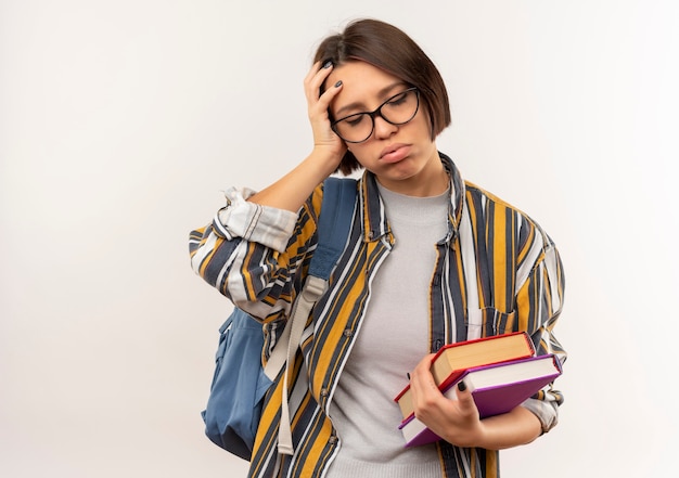 Fatigué de jeune fille étudiante portant des lunettes et sac à dos tenant des livres mettant la main sur la tête avec les yeux fermés isolé sur fond blanc