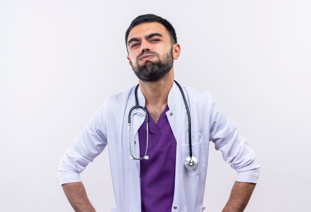 Fatigué jeune homme médecin portant une robe médicale stéthoscope sur mur blanc isolé