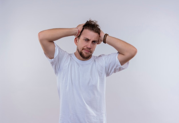 Fatigué de jeune homme vêtu d'un t-shirt blanc a attrapé la tête sur un mur blanc isolé