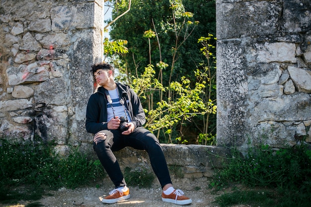 Fatigué jeune photographe assis sur le vieux mur de pierre avec appareil photo