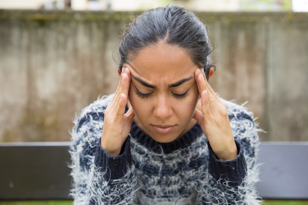 Fatigué jolie jeune femme touchant les temples en plein air