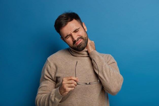 Fatigue mécontente l'homme barbu ressent une gêne dans le cou, a des problèmes de colonne vertébrale