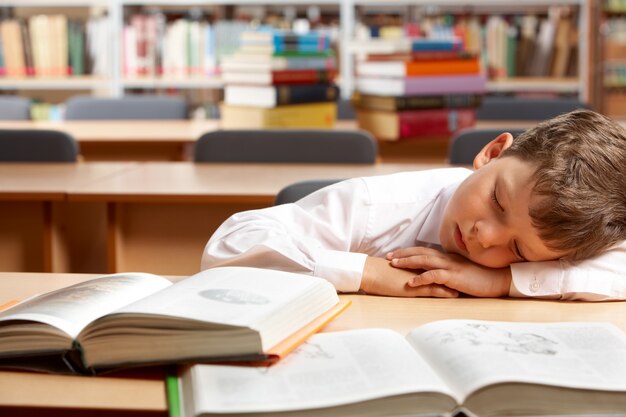 Fatigué petit garçon dort dans la bibliothèque