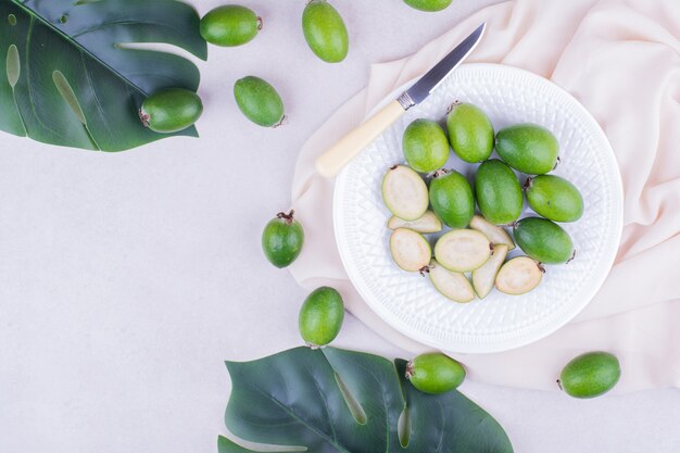 Feijoas verts dans une assiette blanche avec des feuilles autour