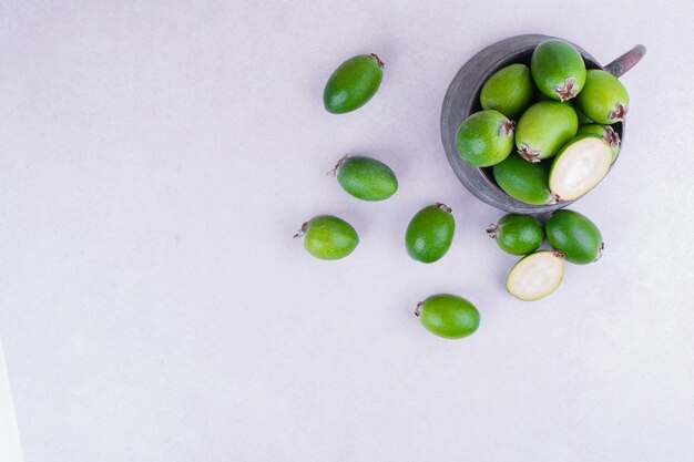 Feijoas verts dans un pot métallique sur une surface blanche