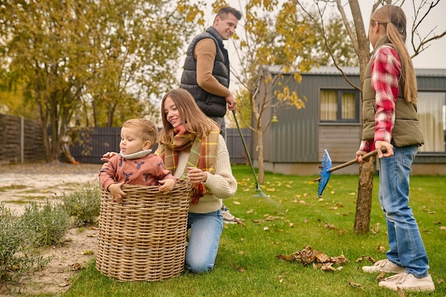 Photo gratuite femme accroupie touchant l'enfant dans le panier et la famille dans le jardin