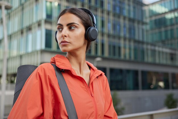 Une femme active sportive concentrée à distance avec une expression réfléchie porte un tapis de fitness roulé se prépare pour des poses d'entraînement à l'extérieur sur fond de ville. Les femmes athlétiques font régulièrement de l'exercice