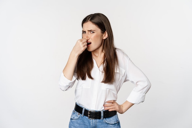 Femme adulte dégoûtée ans fermer le nez de l'aversion et du dégoût mauvaise odeur debout sur fond blanc...