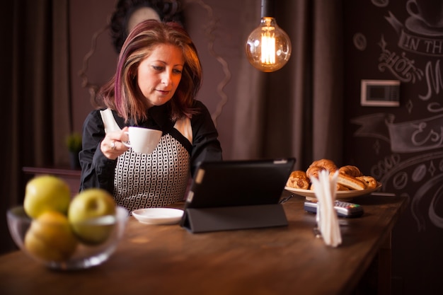 Femme d'affaires adulte recherchant sur sa tablette dans un café vintage. À côté d'un bol de pommes vertes