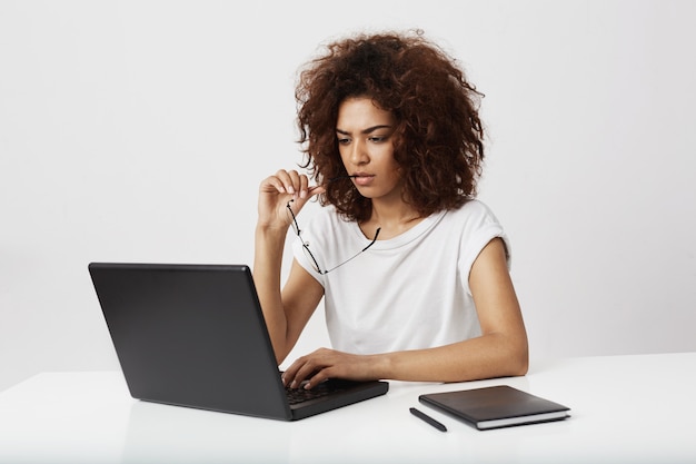 Femme d'affaires africaine regardant écran d'ordinateur portable réfléchissant sur le mur blanc.