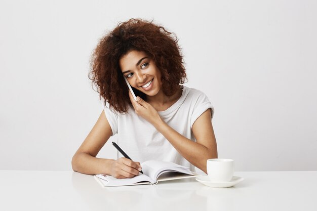 Femme d'affaires africaine souriant parlant au téléphone sur le lieu de travail. mur blanc.