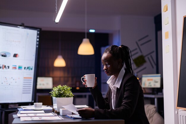 Femme d'affaires afro-américaine bourreau de travail analysant les statistiques de marketing sur la paperasse