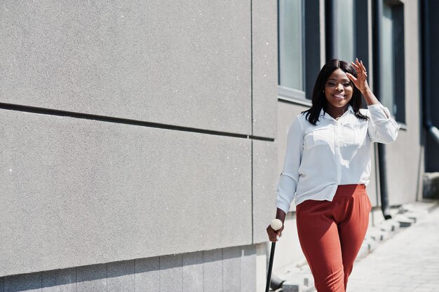 Femme d'affaires afro-américaine formellement habillée en chemisier blanc et pantalon rouge avec une canne à portée de main