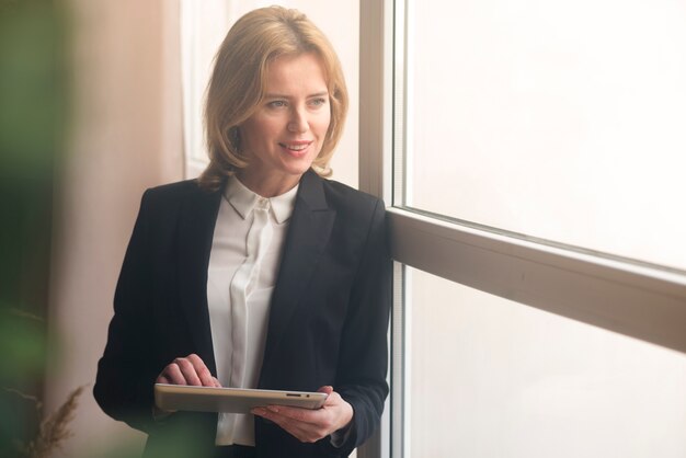 Femme d&#39;affaires à l&#39;aide de tablette à la fenêtre