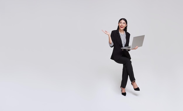 femme d'affaires asiatique heureuse souriante alors qu'elle utilise un ordinateur portable assis sur une chaise blanche