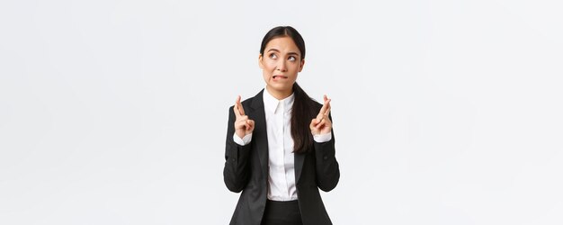 Photo gratuite une femme d'affaires asiatique pleine d'espoir qui a l'air inquiète de se mordre la lèvre et de croiser les doigts bonne chance en faisant un souhait antic