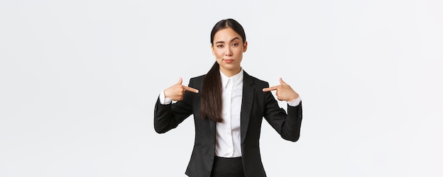 Femme d'affaires asiatique professionnelle en costume se montrant comme offrant les meilleures offres Une vendeuse fière et confiante suggère une aide personnelle ou une assistance debout sur fond blanc