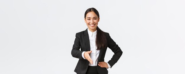 Une femme d'affaires asiatique souriante et confiante tend la main pour une poignée de main ferme saluant un client ou un partenaire commercial pour signer un accord à la recherche d'un arrière-plan blanc debout déterminé et prêt