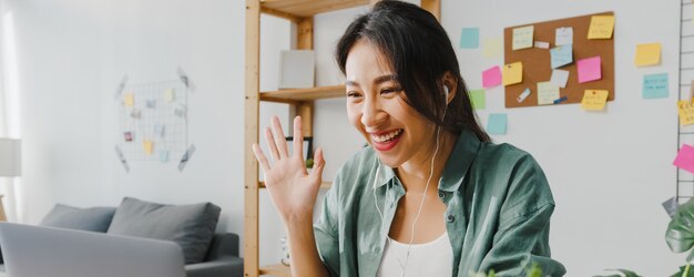 Une femme d'affaires asiatique utilisant un ordinateur portable parle à ses collègues du plan lors d'un appel vidéo tout en travaillant intelligemment à domicile dans le salon.