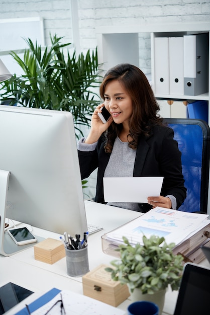 Femme d'affaires asiatiques assis dans le bureau, tenant le document et parler au téléphone mobile