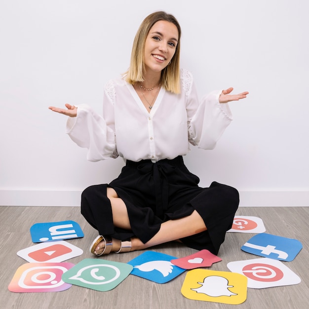 Femme d&#39;affaires assis sur le sol avec des icônes de médias sociaux, haussant les épaules