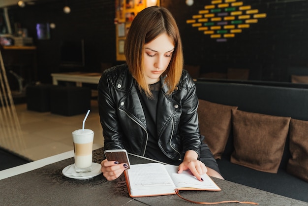 Femme d&#39;affaires au café garde le téléphone en train de planifier sa semaine dans un cahier.