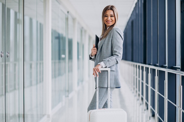 Femme d'affaires avec des bagages de voyage à l'aéroport, tenant un ordinateur portable