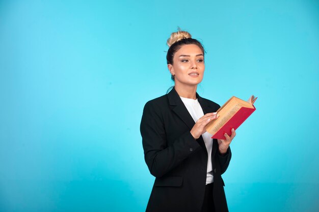 Femme d'affaires en blazer noir avec un livre rouge.