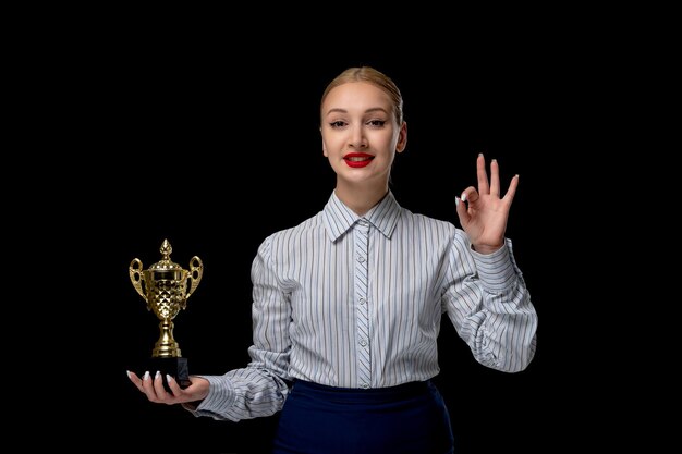 Femme d'affaires blonde jolie fille montrant signe ok avec trophée portant du rouge à lèvres en costume de bureau