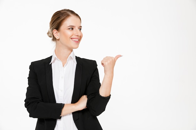 Femme d'affaires blonde souriante regardant et pointant loin sur blanc