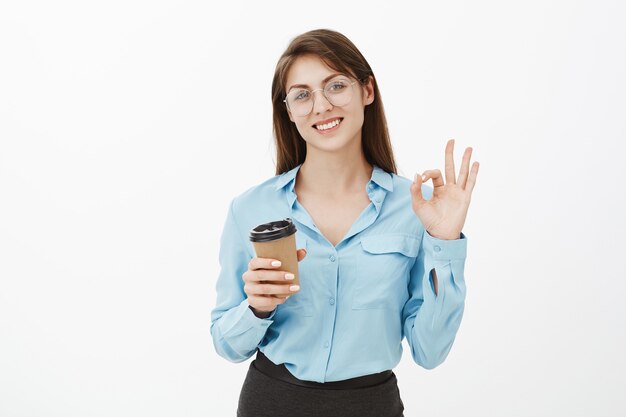 Femme d'affaires brune sympathique posant dans le studio avec son café