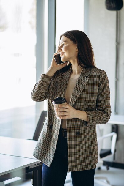 Femme d'affaires buvant du café et utilisant le téléphone au bureau