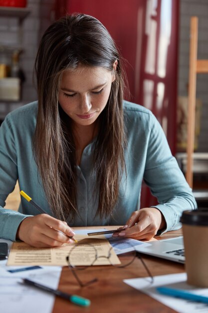 Une femme d'affaires concentrée trie les papiers, crée un projet de démarrage, tient des cartes en plastique, note le nombre