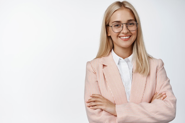 Femme d'affaires confiante et professionnelle croisant les bras sur la poitrine, regardant la caméra avec assurance et souriant debout sur fond blanc