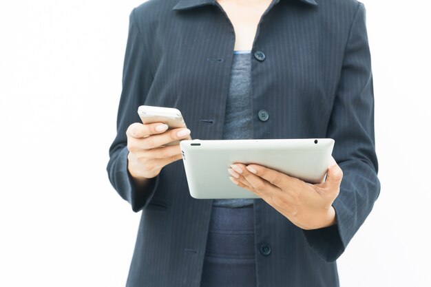 Femme d&#39;affaires en costume sombre en utilisant sa tablette et son téléphone mobile sur fond blanc avec copie