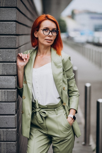 Femme d'affaires en costume vert debout près du mur