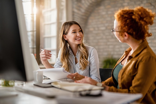 Photo gratuite femme d'affaires créative souriante passant par la paperasse et parlant à sa collègue au bureau