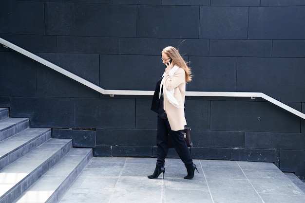 Femme d'affaires dans un manteau avec un sac dans ses mains monte les marches du bâtiment. Le concept de carrière et d'entreprise