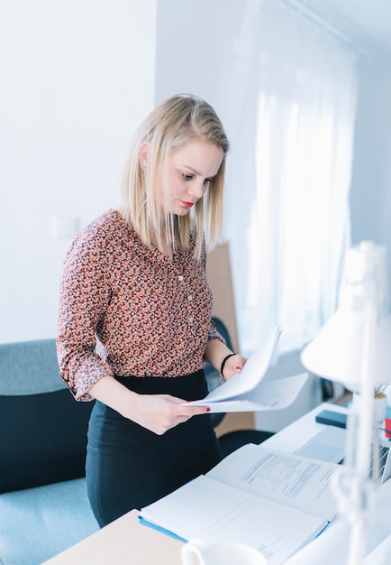 Femme affaires, debout, près, bureau, lecture documents