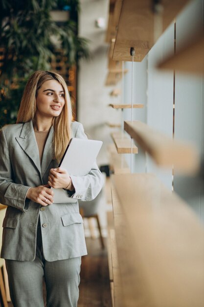 Femme d'affaires debout près de la fenêtre et tenant un ordinateur